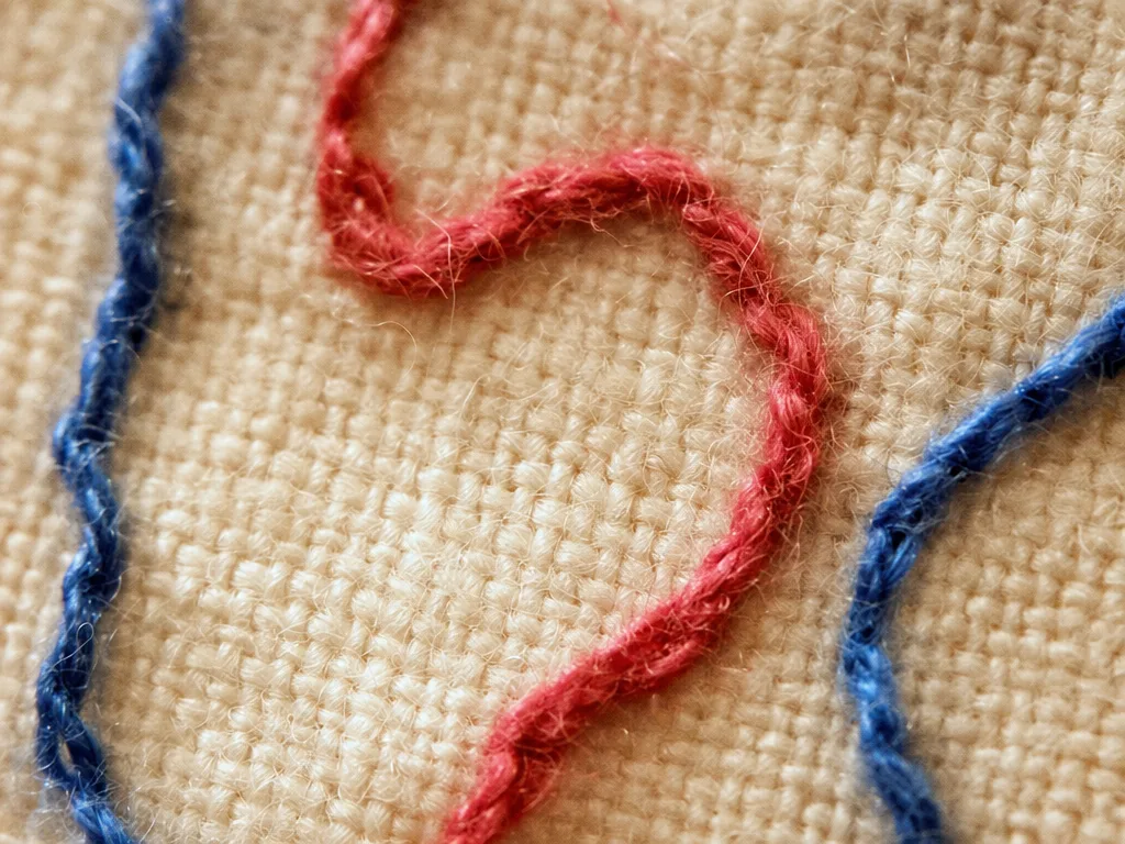 Detaliu macro: cusături de broderie cu ață colorată pe in crem